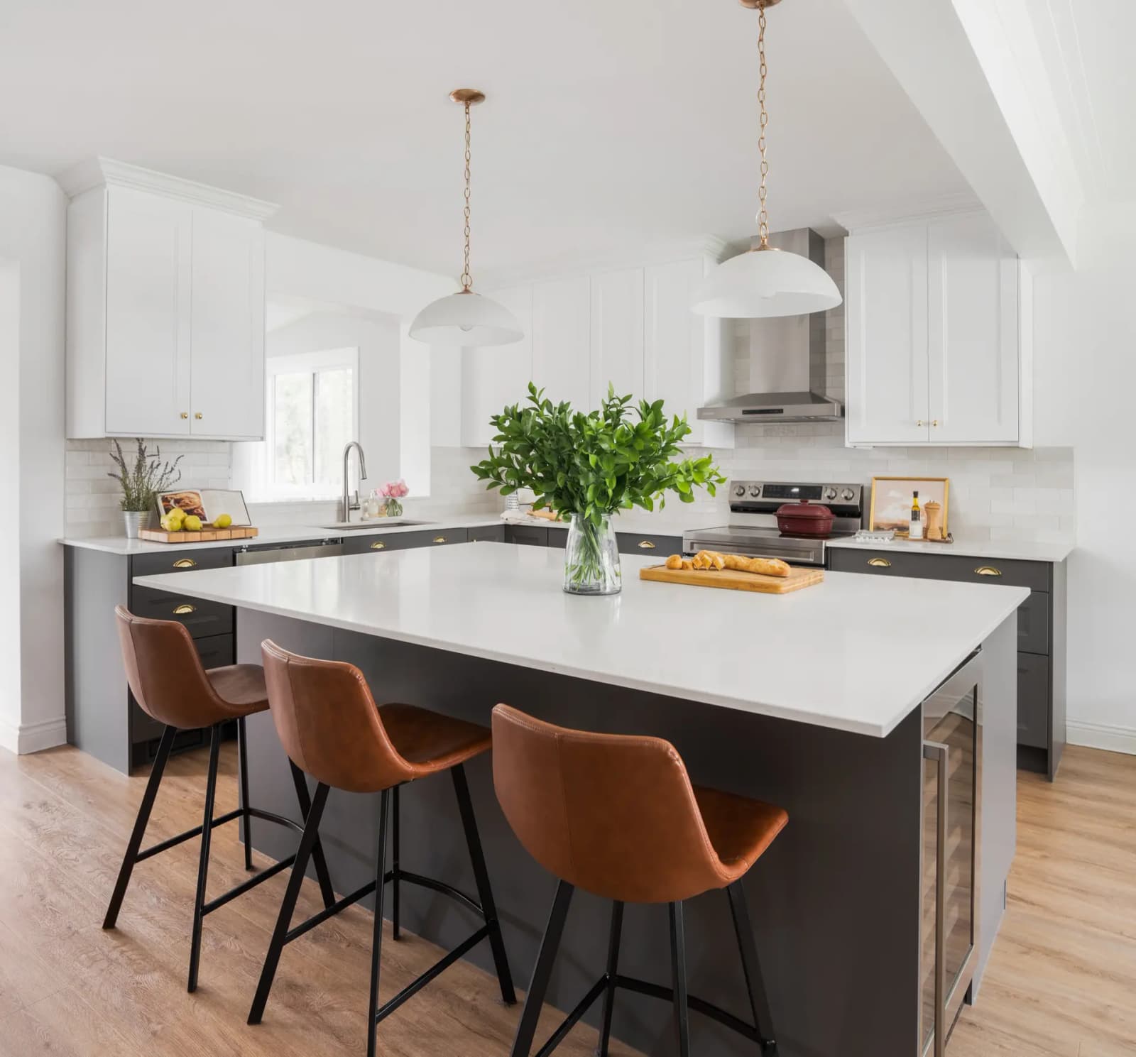 Transitional-style kitchen in Montreal, featuring a matte black central island with a white quartz countertop. White shaker cabinets and copper handles bring an elegant touch to the space. The light wood flooring and brown leather stools create a warm, welcoming vibe Select an Image Source: MTL Contractors