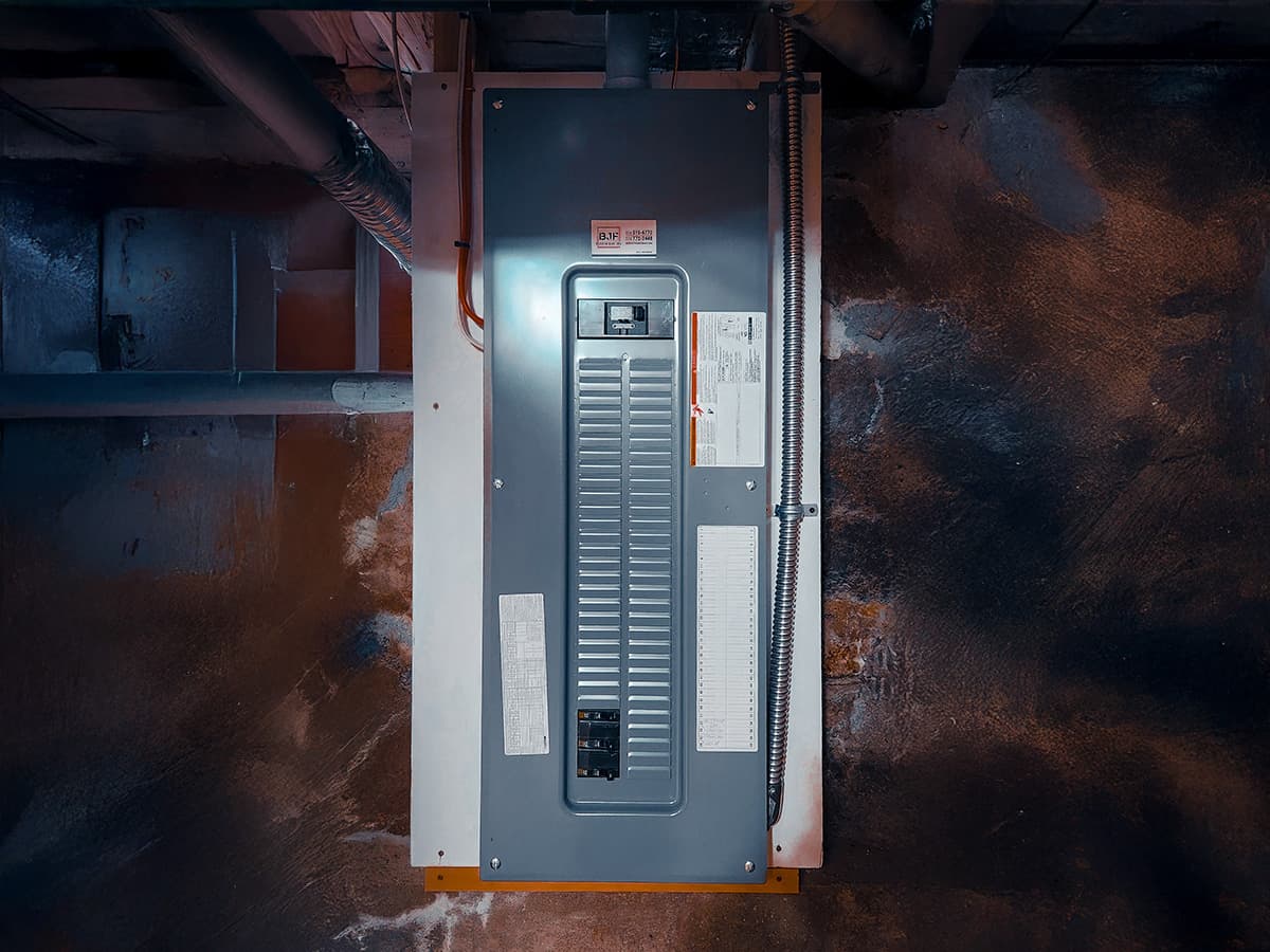 Residential electrical panel installed in a basement with exposed wiring and circuit breakers.
