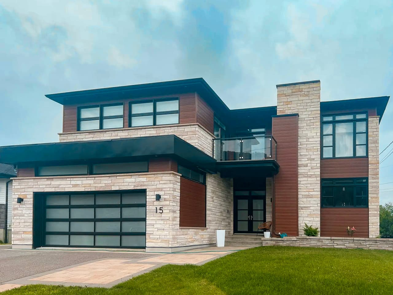 Contemporary two-story house with stone and wood façade, glass garage door, and glass balcony