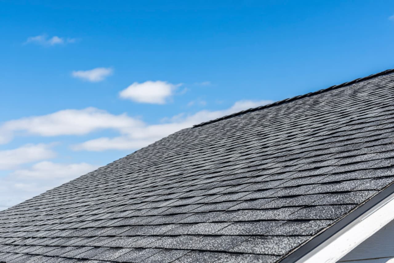 Residential roof with grey asphalt shingles under a clear blue sky