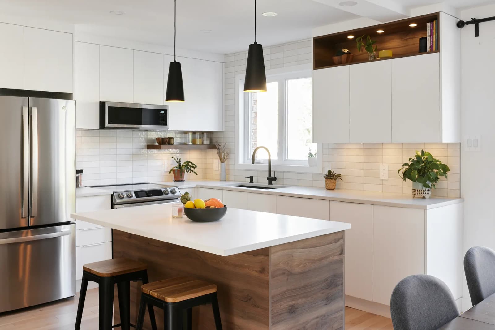 Scandinavian-style Montréal kitchen, featuring a centre island with a natural wood countertop, minimalist white cabinetry, and white subway tile backsplash. The light wood flooring adds a touch of warmth to the space.