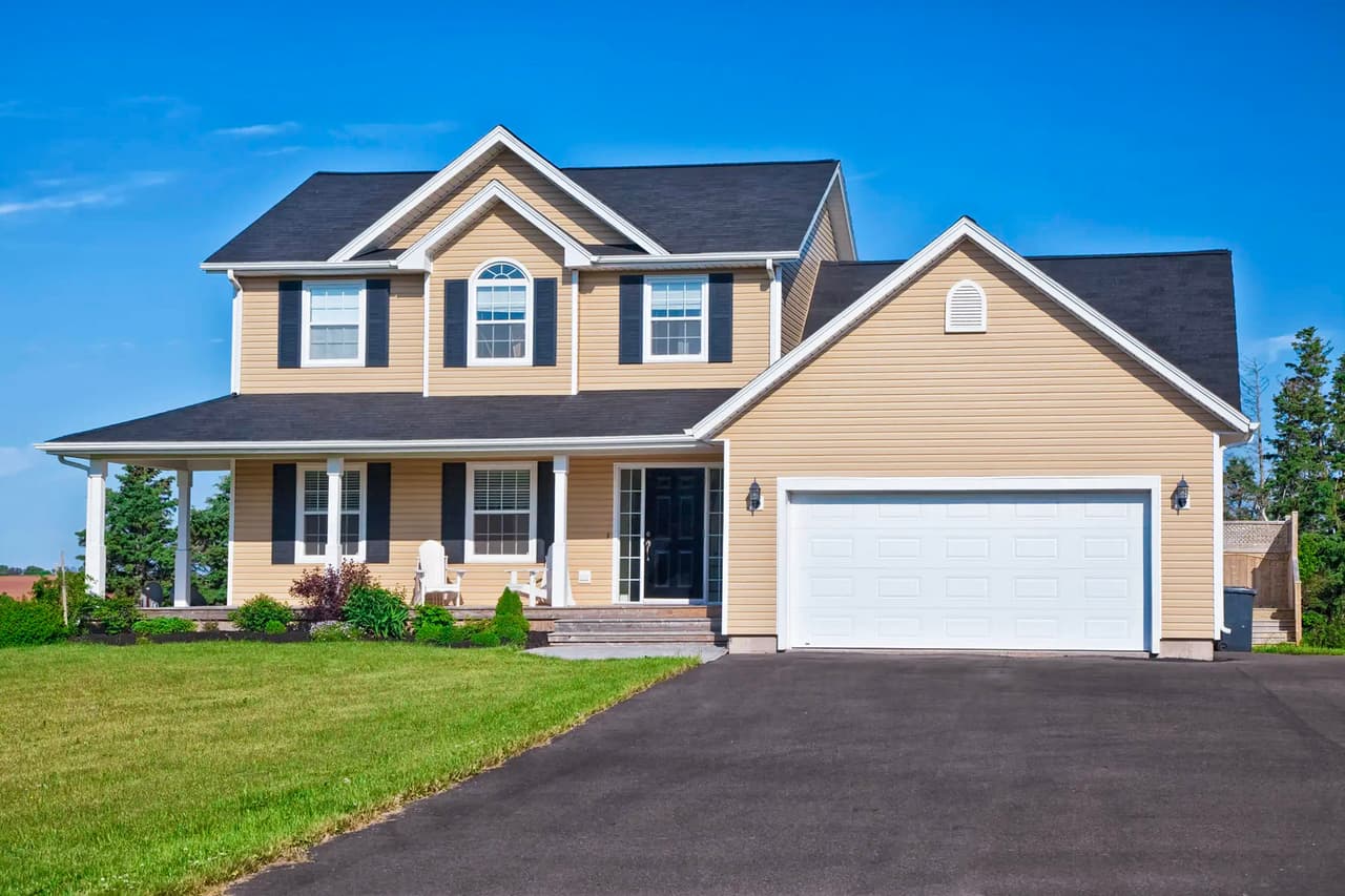 Modern family home with a double garage, newly paved asphalt driveway, and well-maintained landscaping under a blue sky.