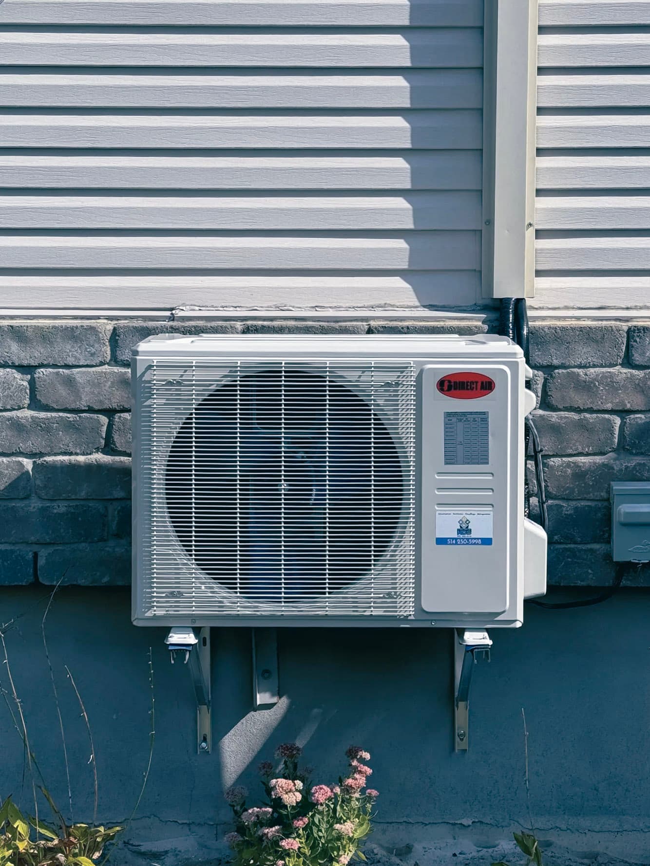 Direct Air outdoor wall-mounted heat pump installed on a stone and vinyl house wall