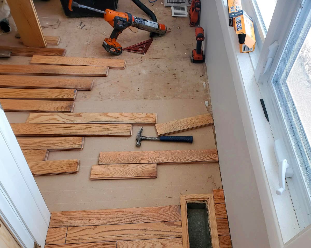 Hardwood flooring installation with construction tools and planks being laid near a window.