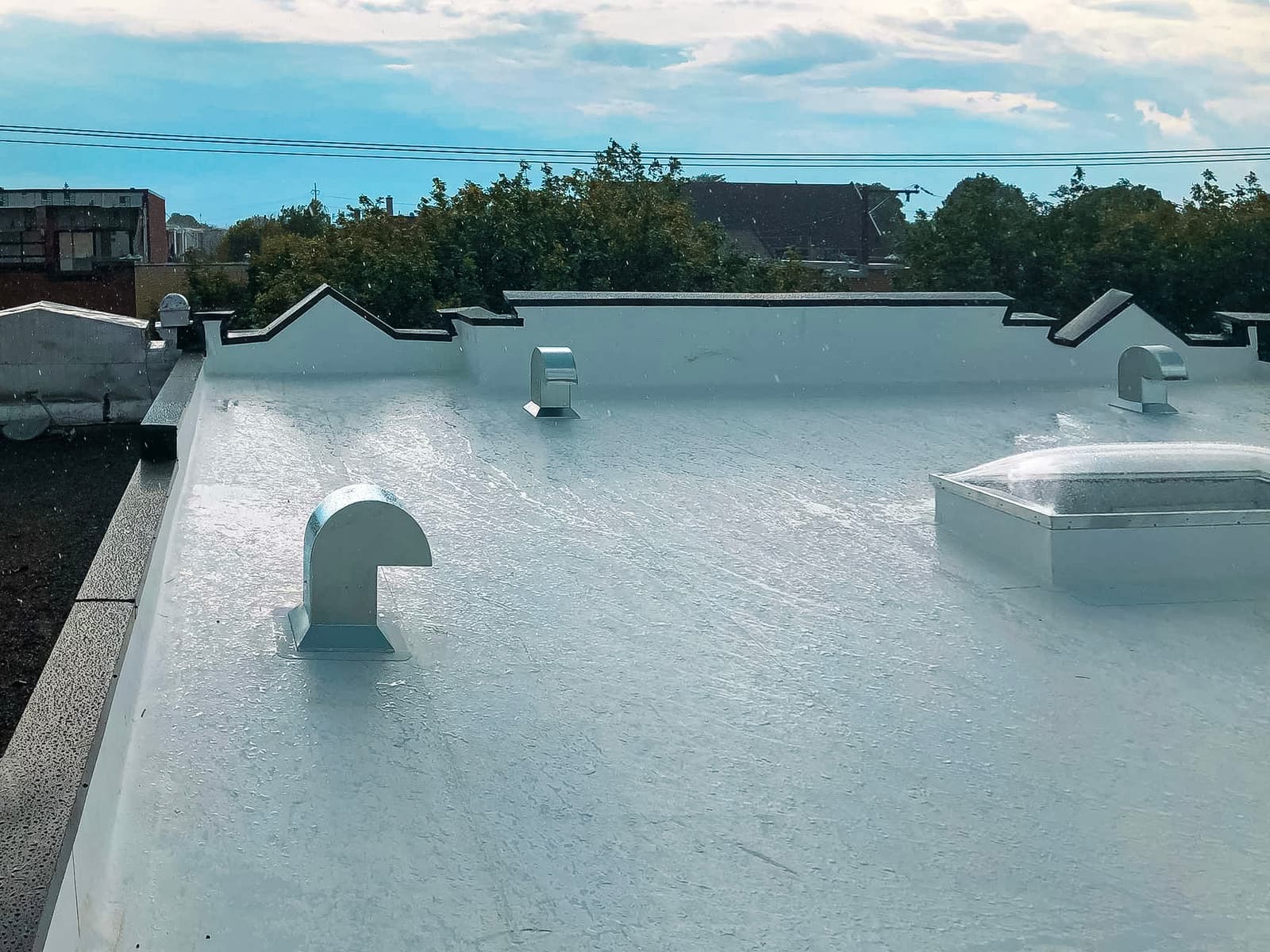 White flat roof with waterproof coating, ventilation openings, and a skylight under the rain.