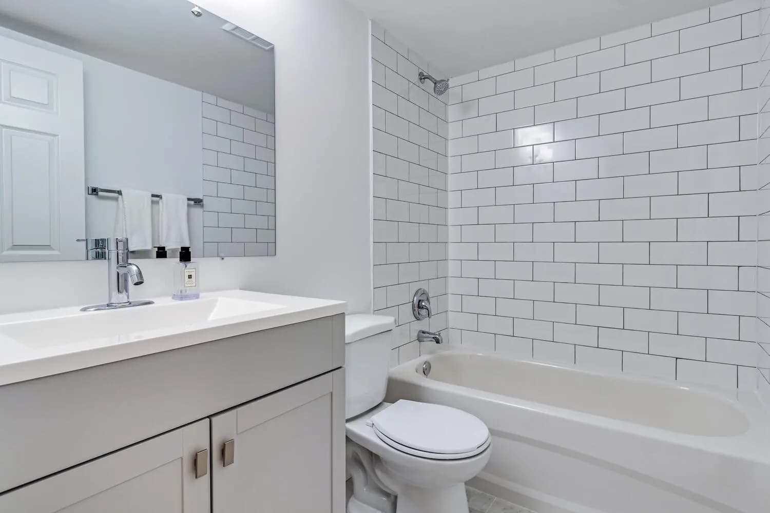 Muted and functional bathroom, featuring a shower tub combo, white tiled walls, and a storage cabinet.
