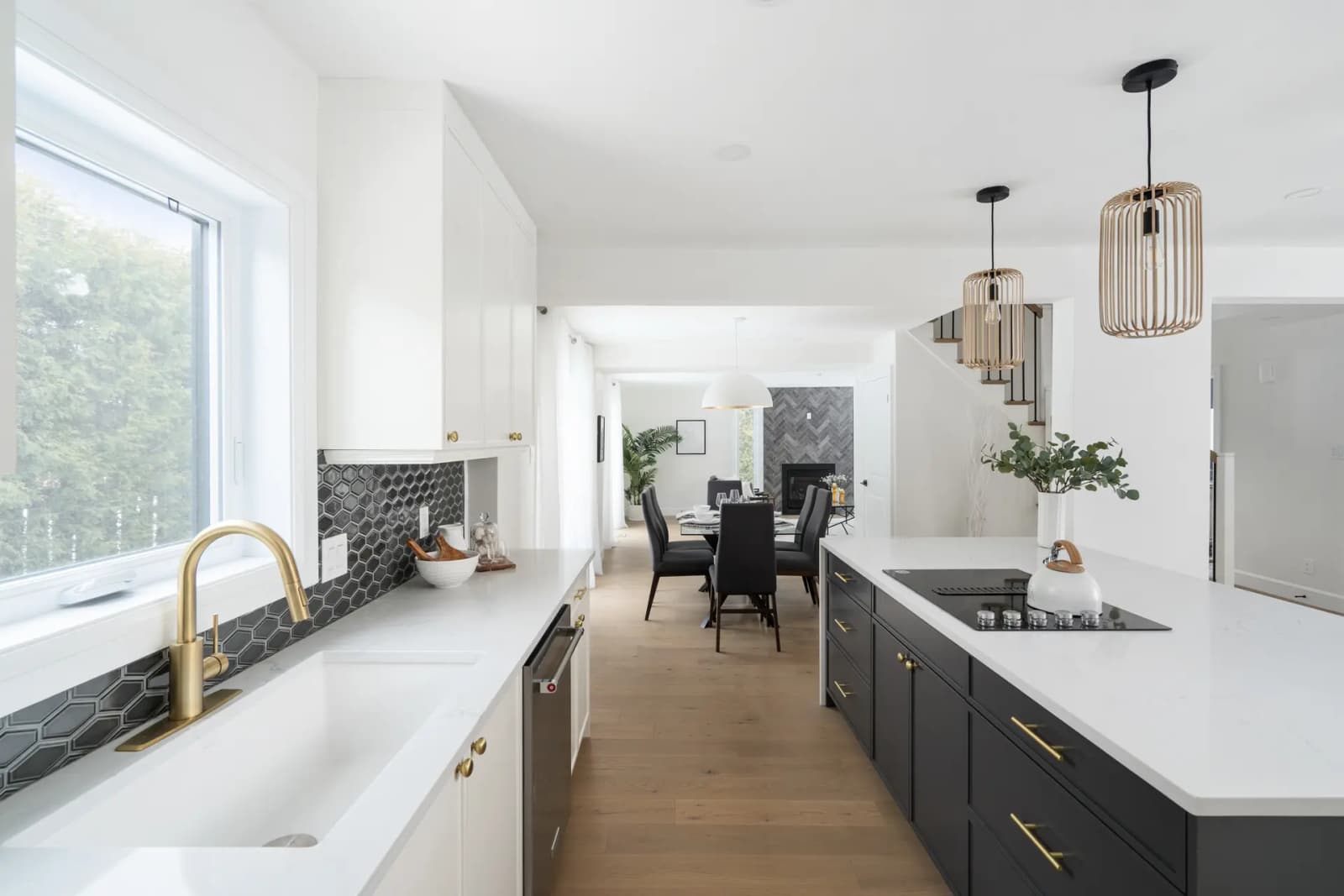 Contemporary-looking Montréal kitchen, featuring a matte black central island with a white quartz countertop. The white shaker cabinets and brass handles add a touch of elegance to the space, while the light wood flooring and pendant lights make for a warm, inviting setting.