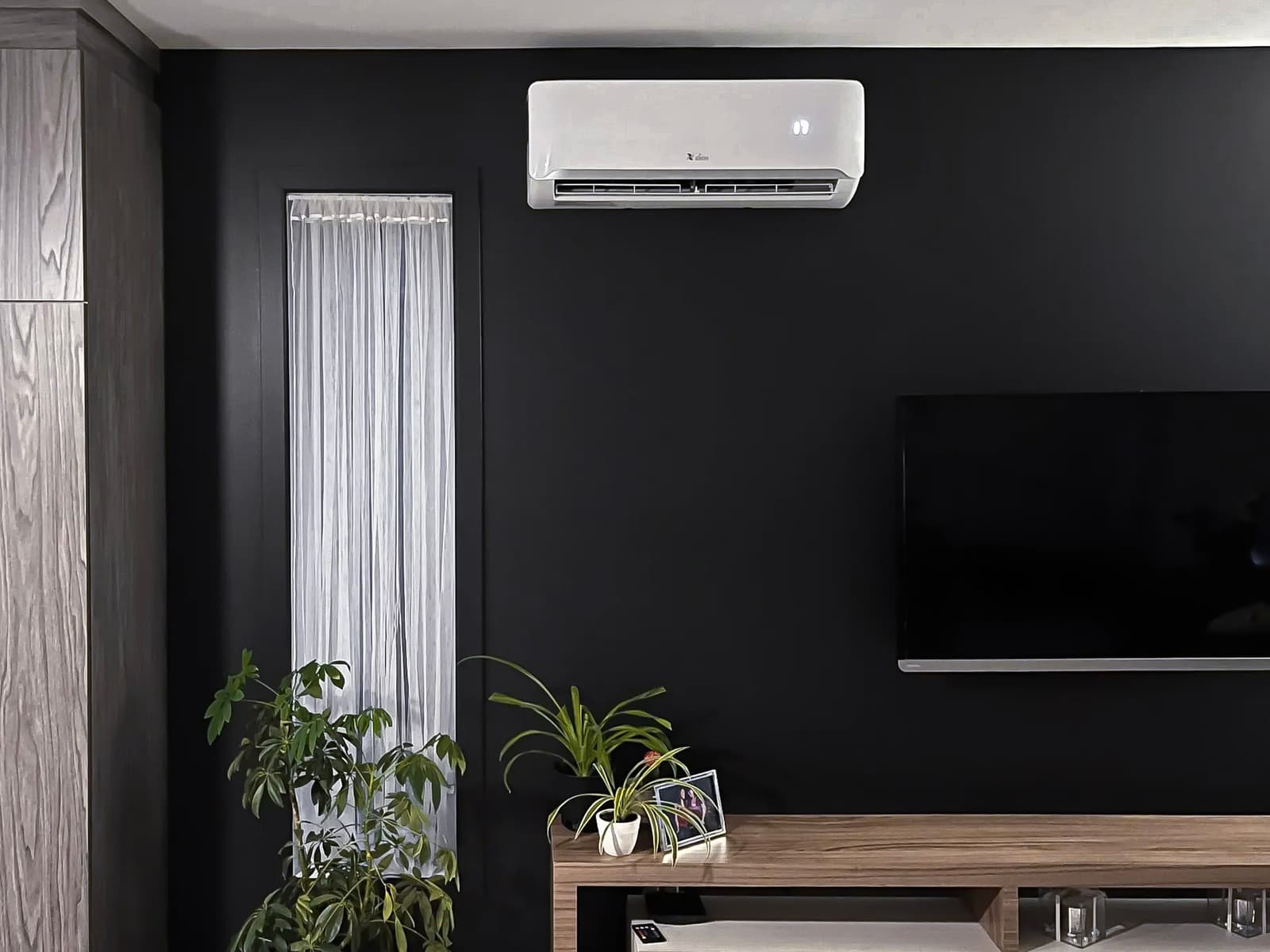 White wall-mounted air conditioner in a modern living room with black wall and wooden TV stand