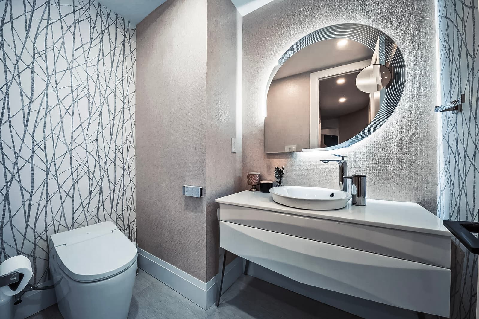 Modern bathroom with smart toilet, minimalist white vanity, backlit oval mirror, and abstract patterned accent wall.