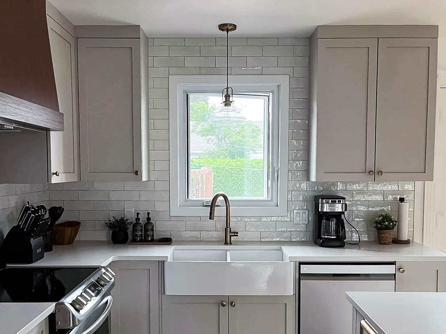 Modern kitchen with gray cabinets, white countertops, farmhouse sink, and stainless steel appliances, illuminated by a glass pendant light