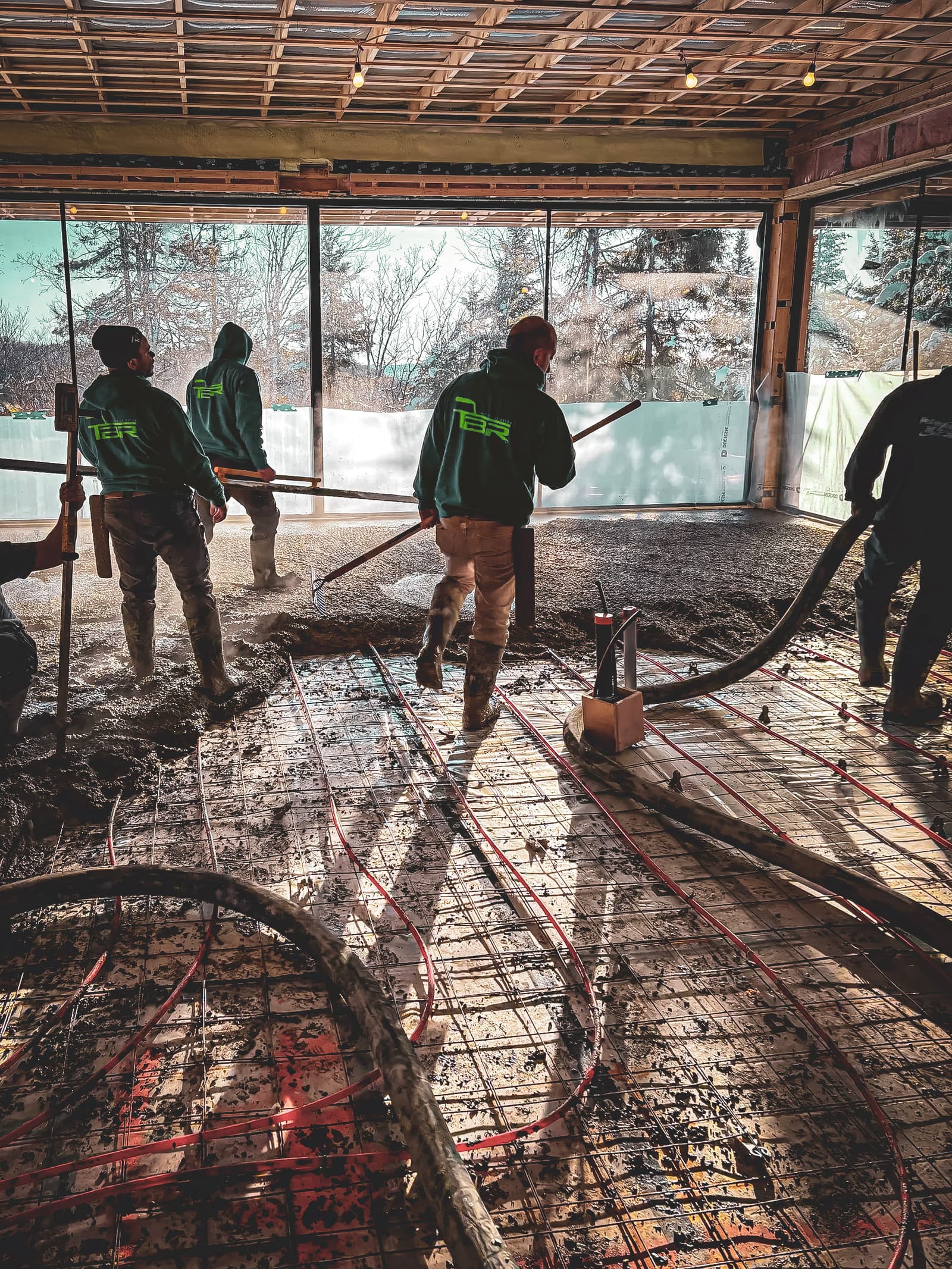  Workers pouring a concrete slab in a building under construction with a visible underfloor heating system.