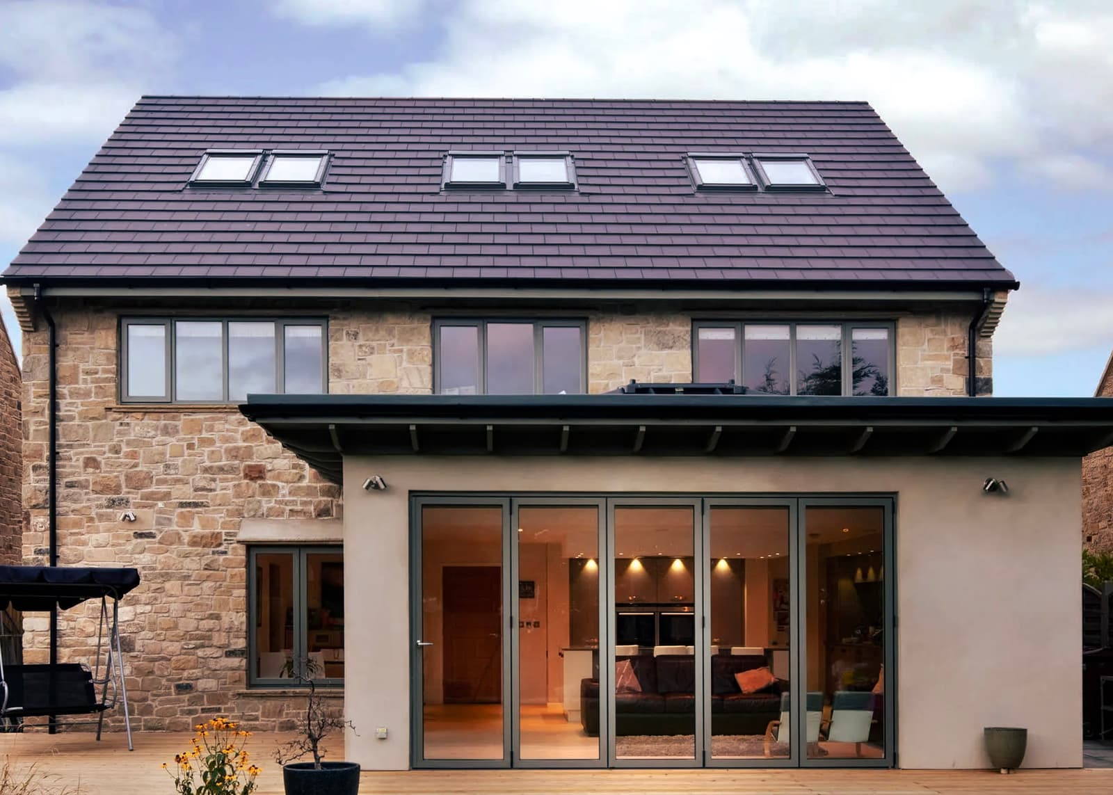 Renovated stone house with tiled roof, double-glazed windows, folding patio doors, wooden deck, and modern outdoor lighting.