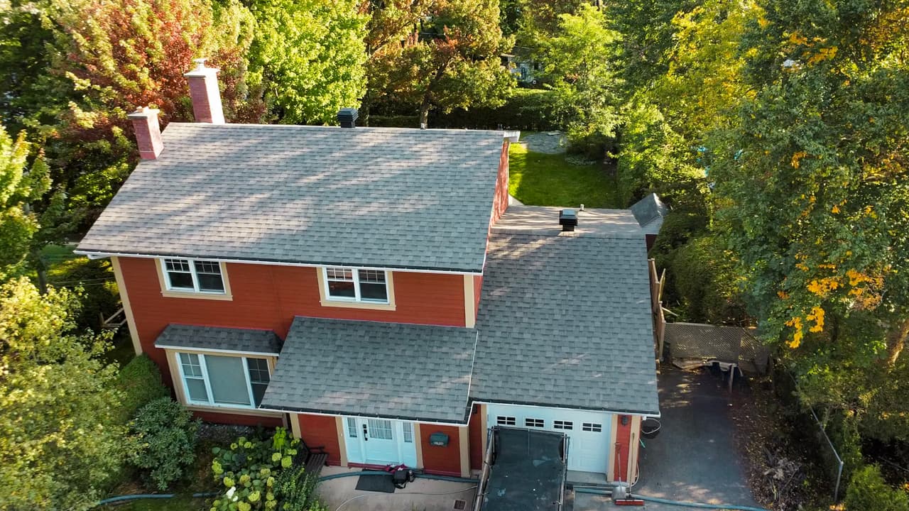 Traditional red house with grey asphalt shingle roof surrounded by greenery