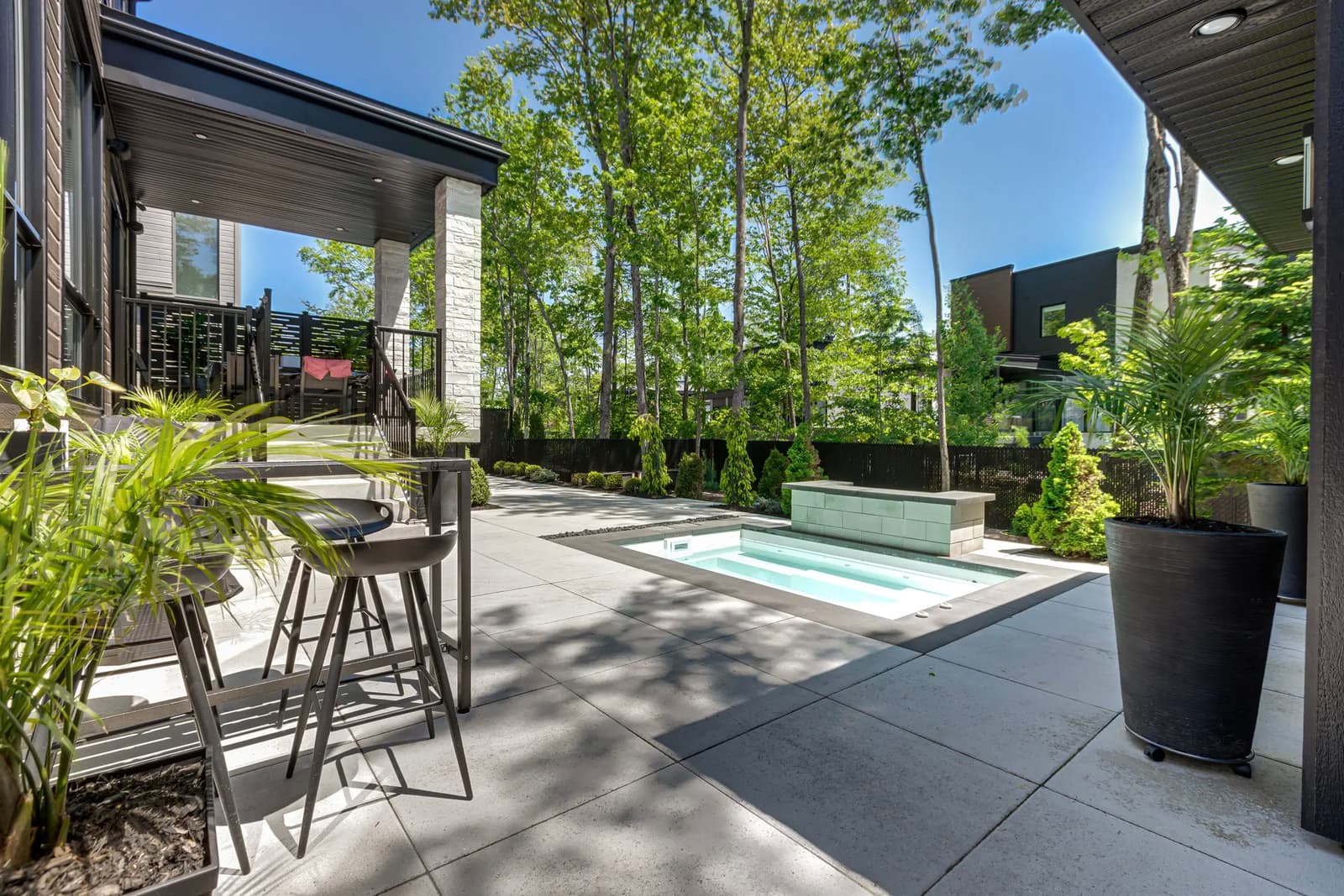 Modern backyard with built-in spa, large concrete patio, outdoor furniture, and lush greenery