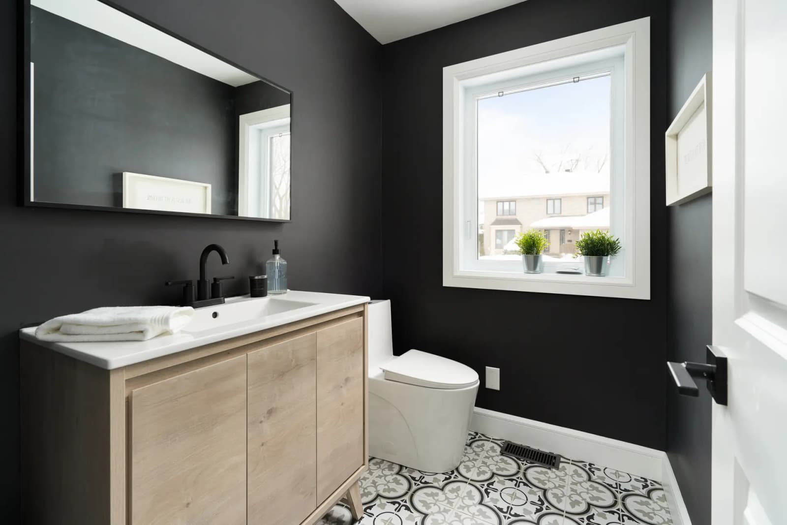 Contemporary bathroom interior with black walls, tiled floor, and a window providing natural light.