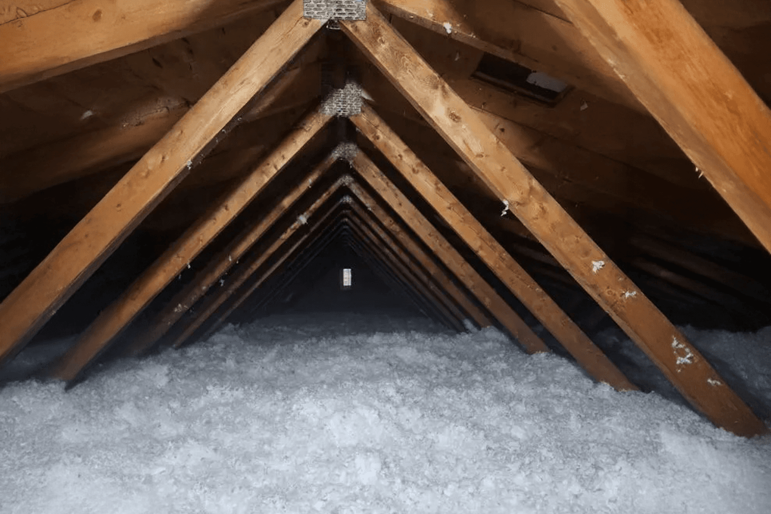Insulated attic with blown-in cellulose under a wooden framework, providing thermal and acoustic protection.