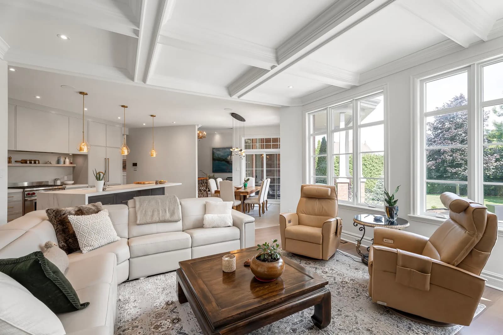 Bright living room with sectional sofa, leather armchairs, and large windows in an open space.