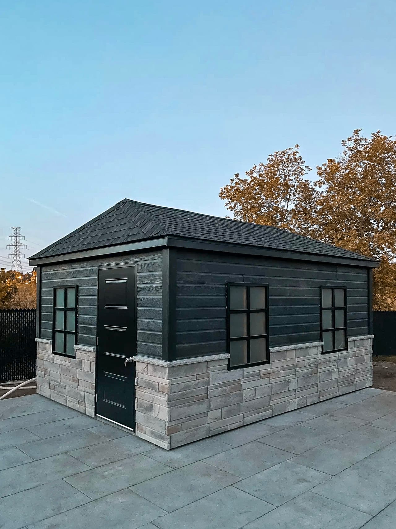 Modern shed with black wood siding and decorative stone base on a concrete slab