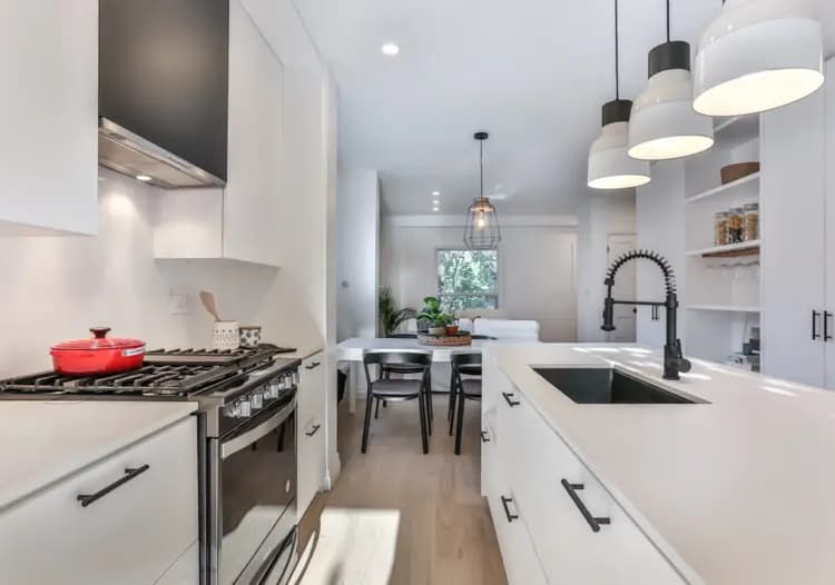 Scandinavian-style kitchen in Montreal, featuring a spacious center island with black barstools, minimalist white cabinets and a geometric mosaic backsplash. The gray ceramic floor adds a touch of warmth to the space.