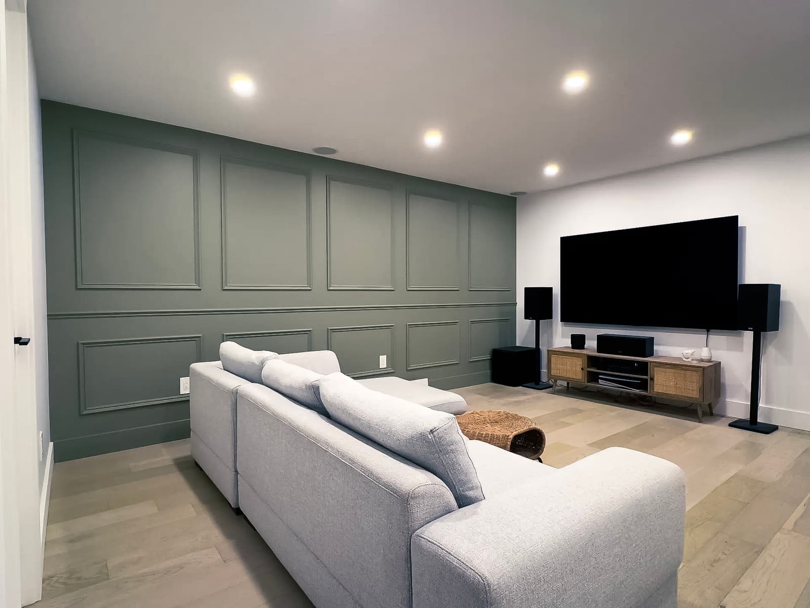Modern living room with a green accent wall, a large gray sofa, a flat-screen TV, and an audio system.