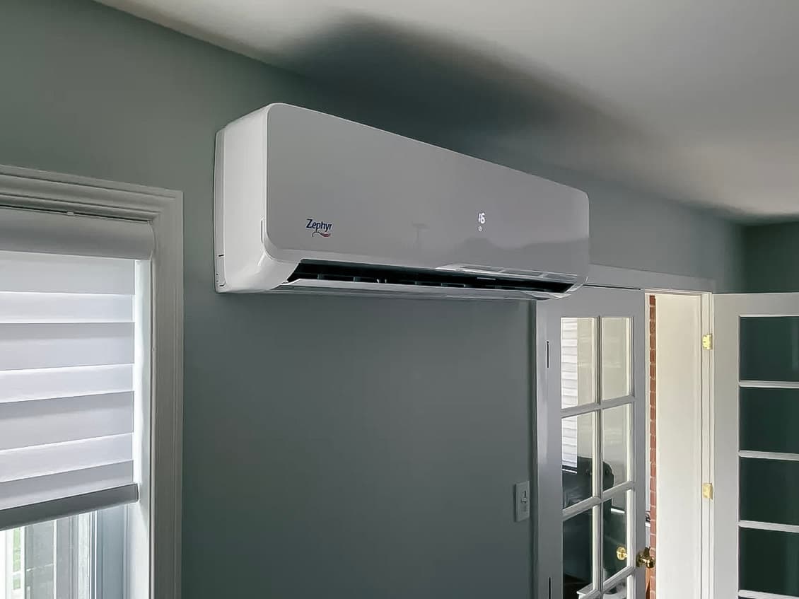 Zephyr wall-mounted air conditioning unit installed in a room with gray walls, a glass door, and a white blind.