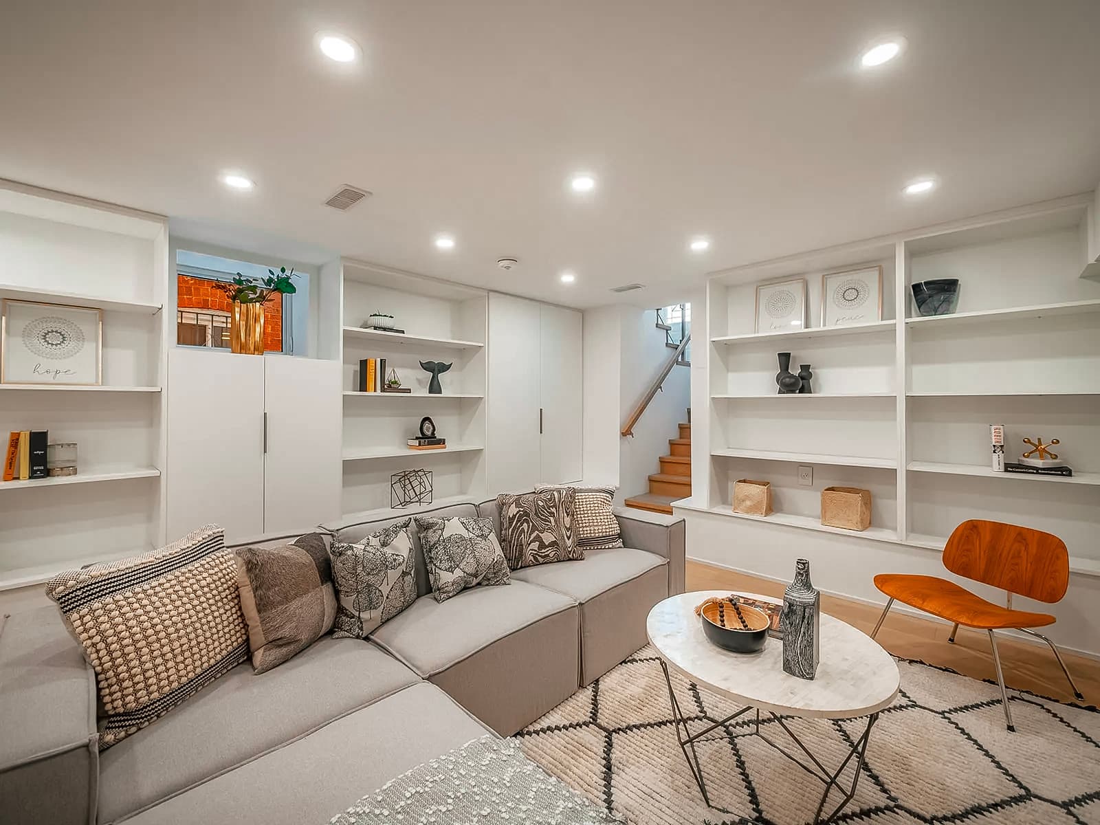 Finished basement with a modern living room featuring a modular sofa, built-in bookshelves, a marble coffee table, a wooden chair, and minimalist decor.