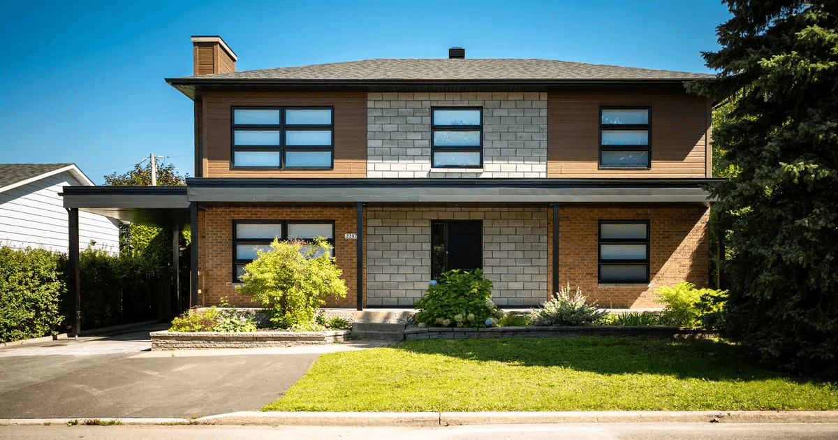 Two-story residential house facade with brick, stone and wood siding, shingle roof, modern windows, asphalt driveway and landscaped front yard