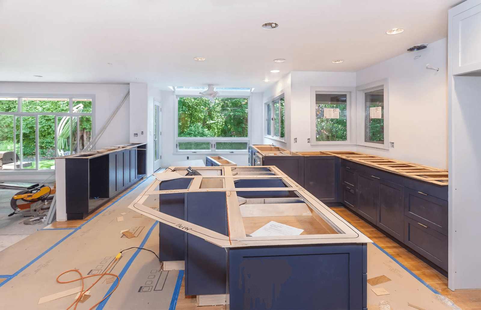 esidential kitchen under renovation with dark blue cabinets being installed, a large central island, multiple windows and countertops awaiting completion