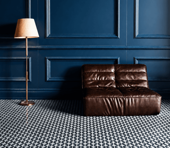 Elegant living room with dark navy paneled wall, brown leather chair, floor lamp and black-and-white geometric tile flooring