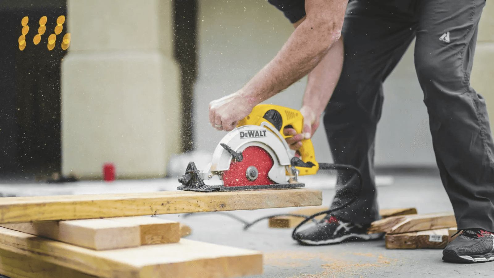 Worker using a circular saw to cut a wooden plank at a construction site.