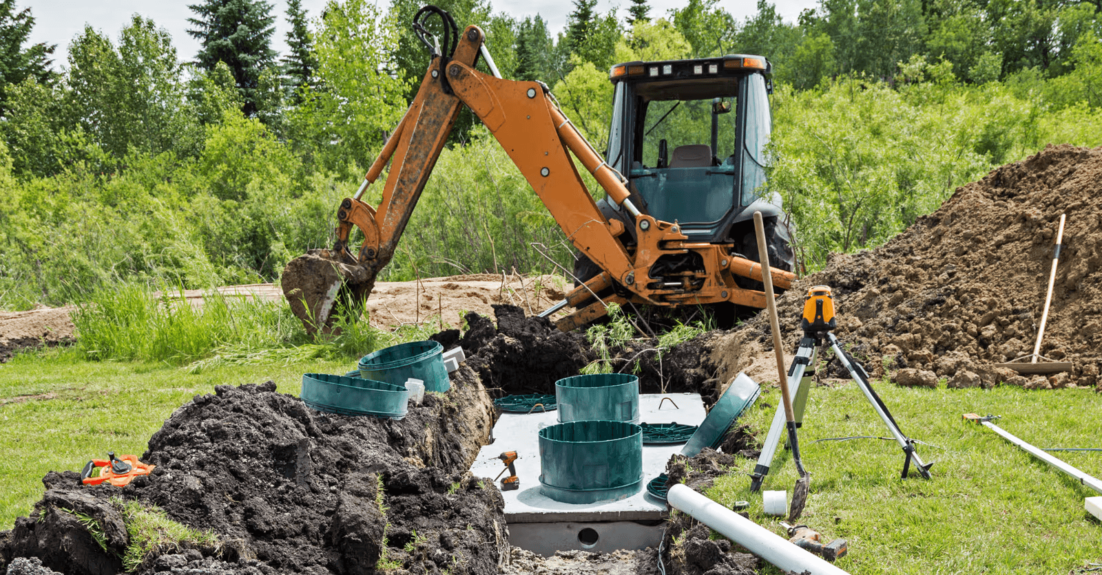 Residential septic tank installation with backhoe, excavation, pipes and leveling equipment on a grassy property.