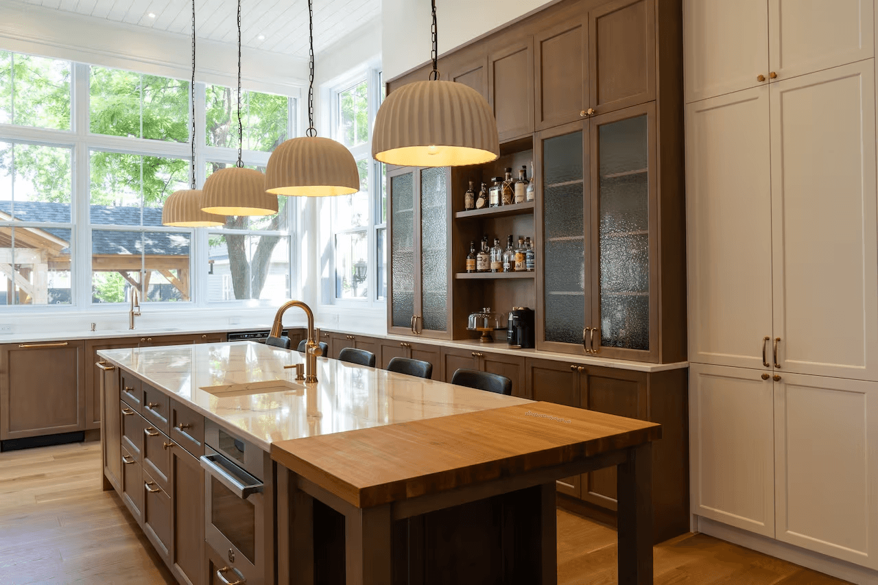 High-end kitchen with custom brown and white cabinetry, large central island, light countertop, pendant lights and oversized windows