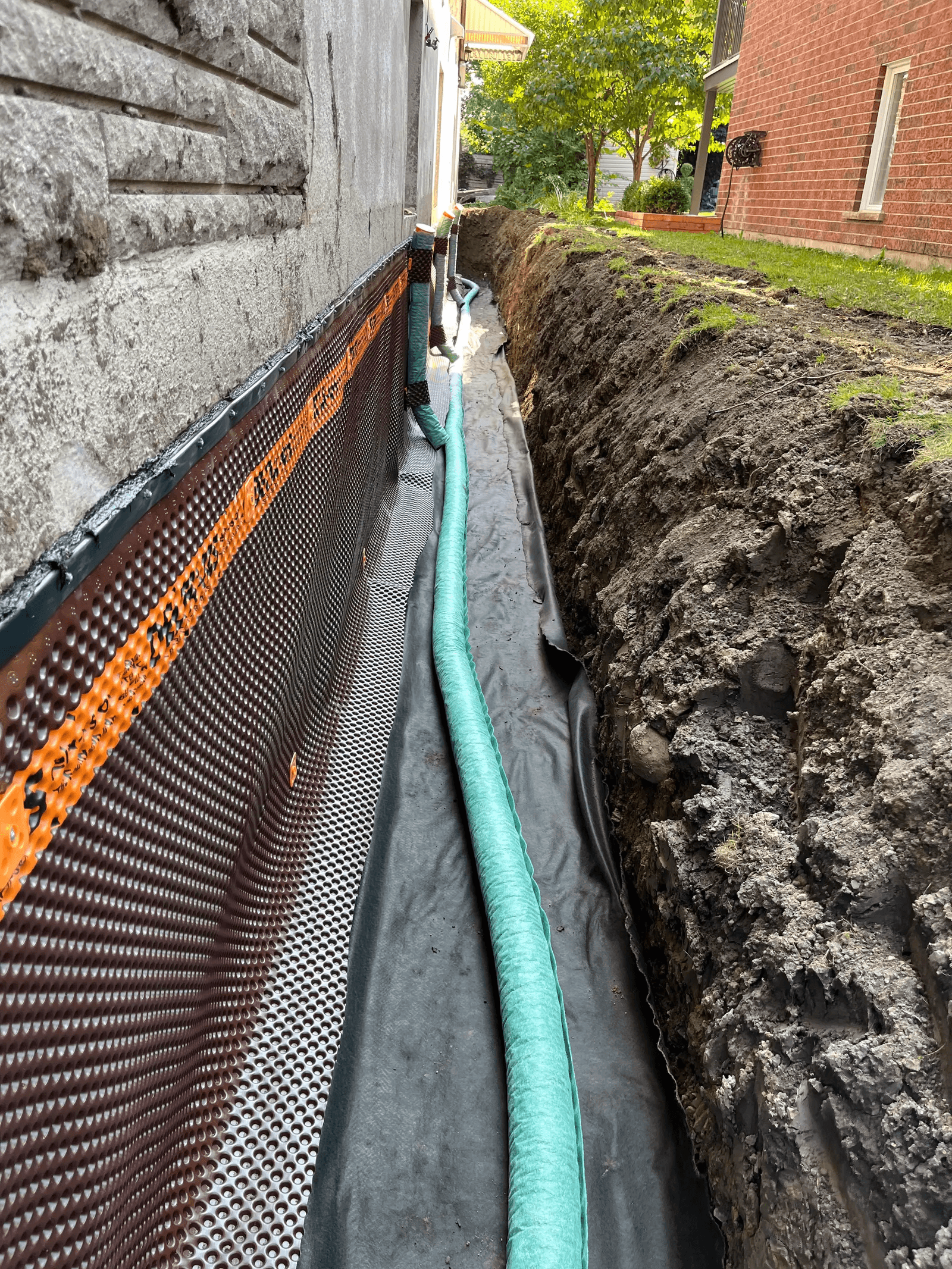 Installation of a French drain with a waterproofing membrane along the foundation of a house.