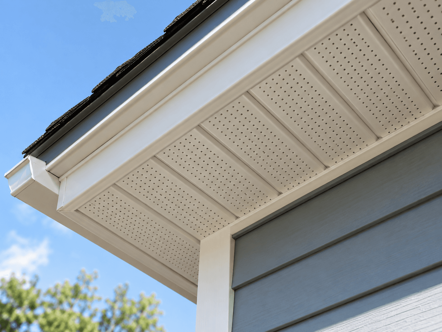 Residential home eaves detail with black roof shingles, white vented soffits, fascia, gutter and downspout over grey exterior siding