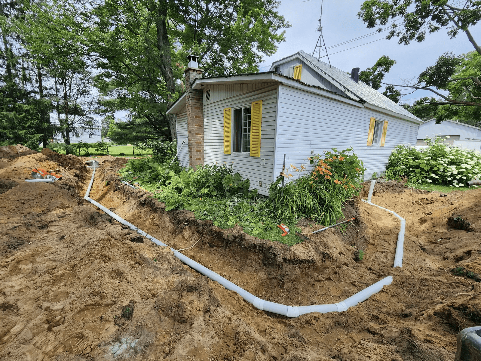 Residential excavation around a house with underground drainage or septic system pipes installed in trenches along the property.
