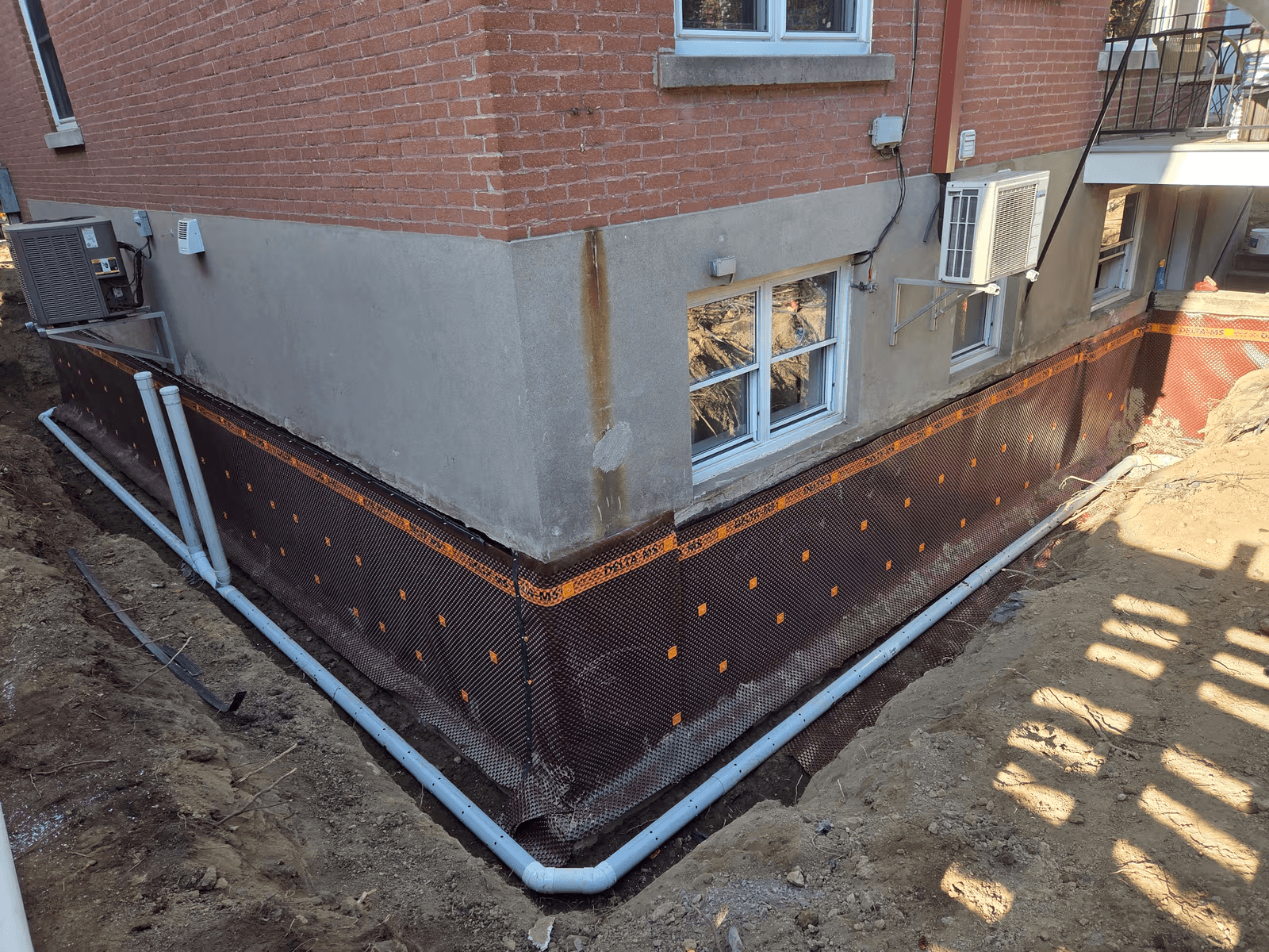 French drain installation around the foundation of a brick house with drainage membrane, perforated pipes and perimeter excavation