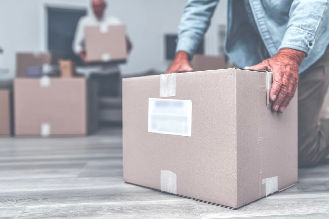 Residential moving with sealed cardboard boxes on modern floor and man carrying a box inside a house.