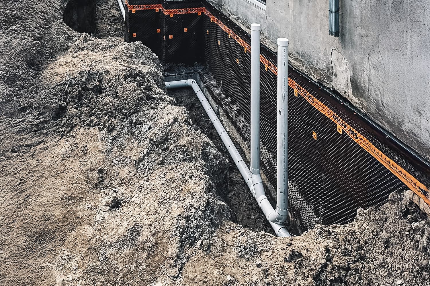 Excavation work for the installation of a French drain and waterproofing membrane on a house foundation.