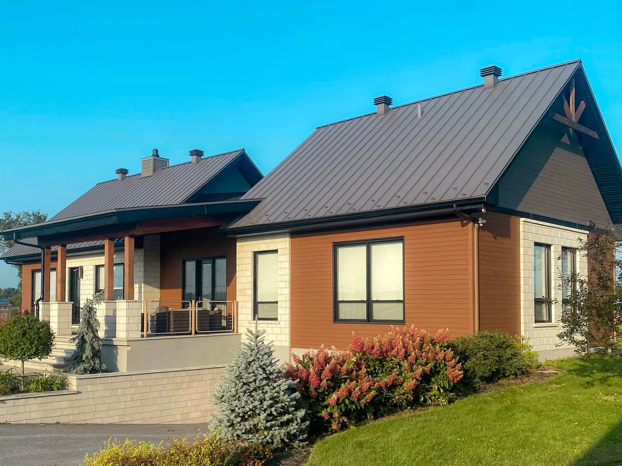 Modern suburban bungalow with metal roofing, mixed wood and masonry cladding, landscaped yard, and covered patio.