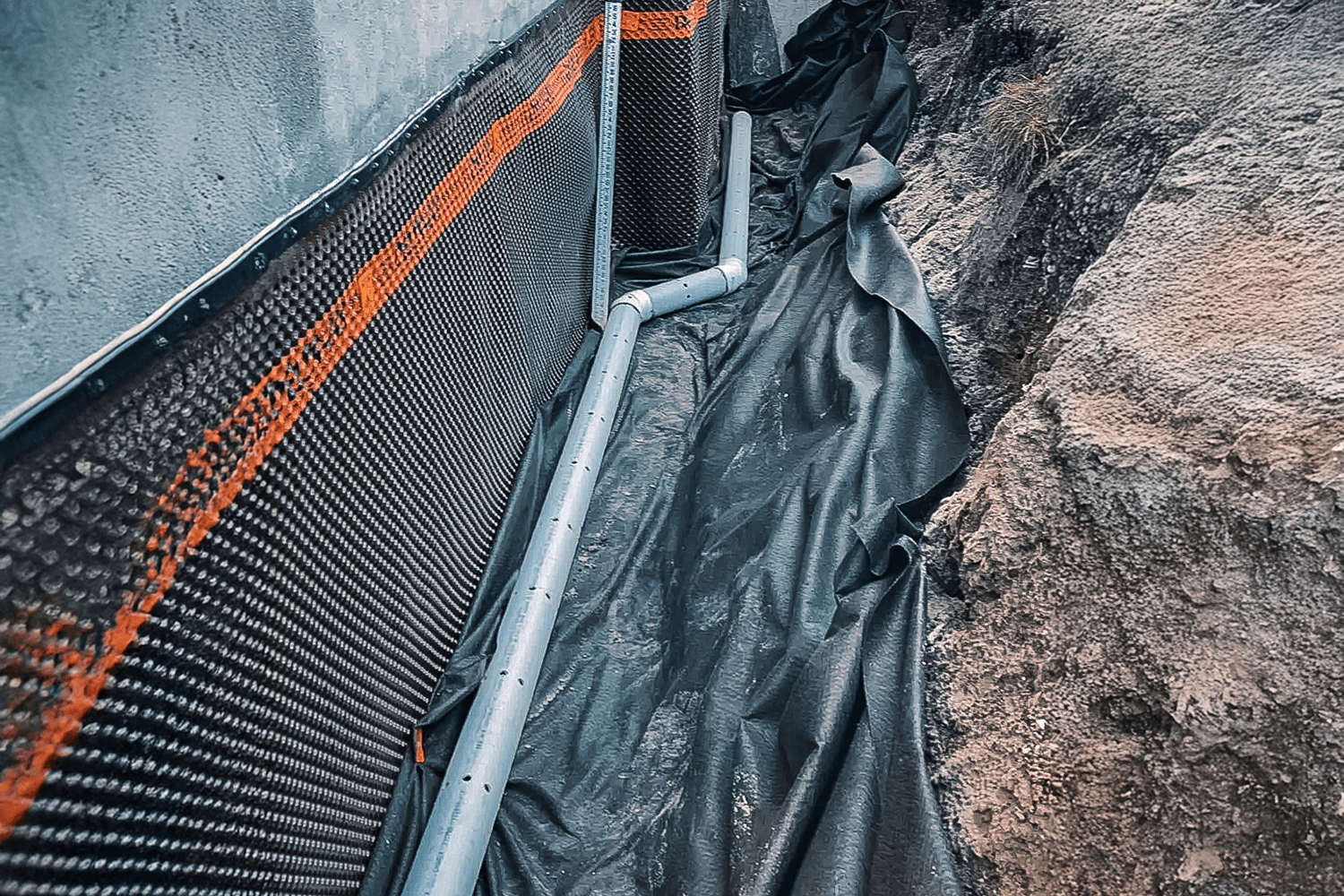 Installation of a French drain with a waterproofing membrane on a house foundation.