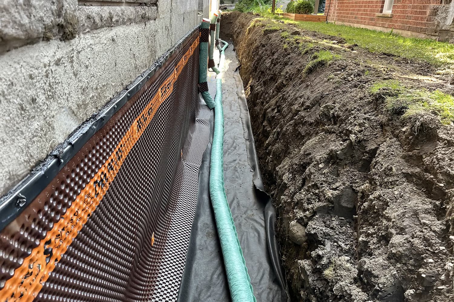 Installation of a French drain with a waterproofing membrane along the foundation of a house.
