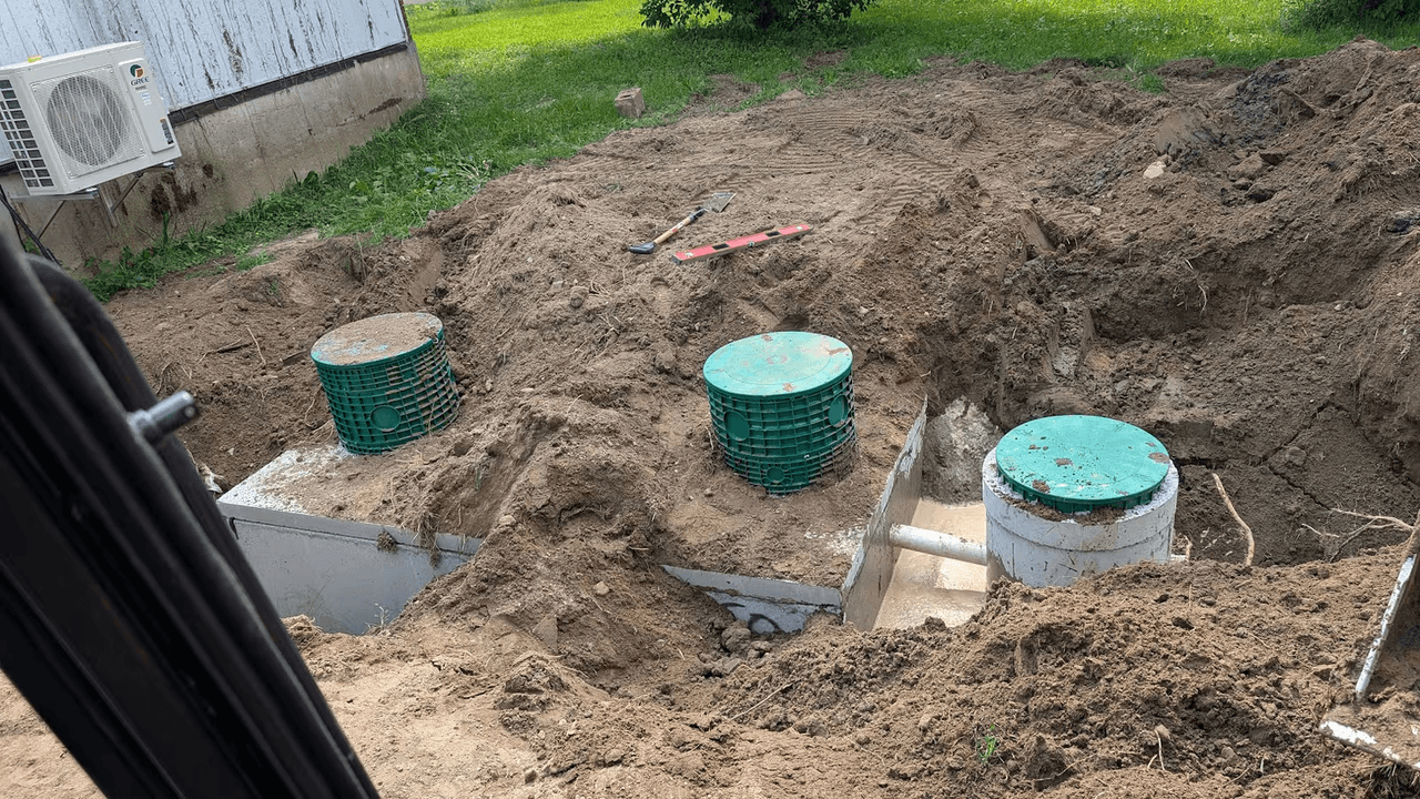 Septic system installation with excavation, access risers and underground pipes near a residential house