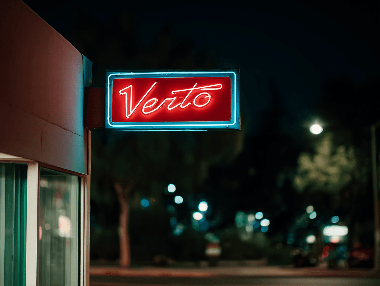 Red and blue neon Verto sign mounted on a commercial storefront and photographed at night in an urban setting