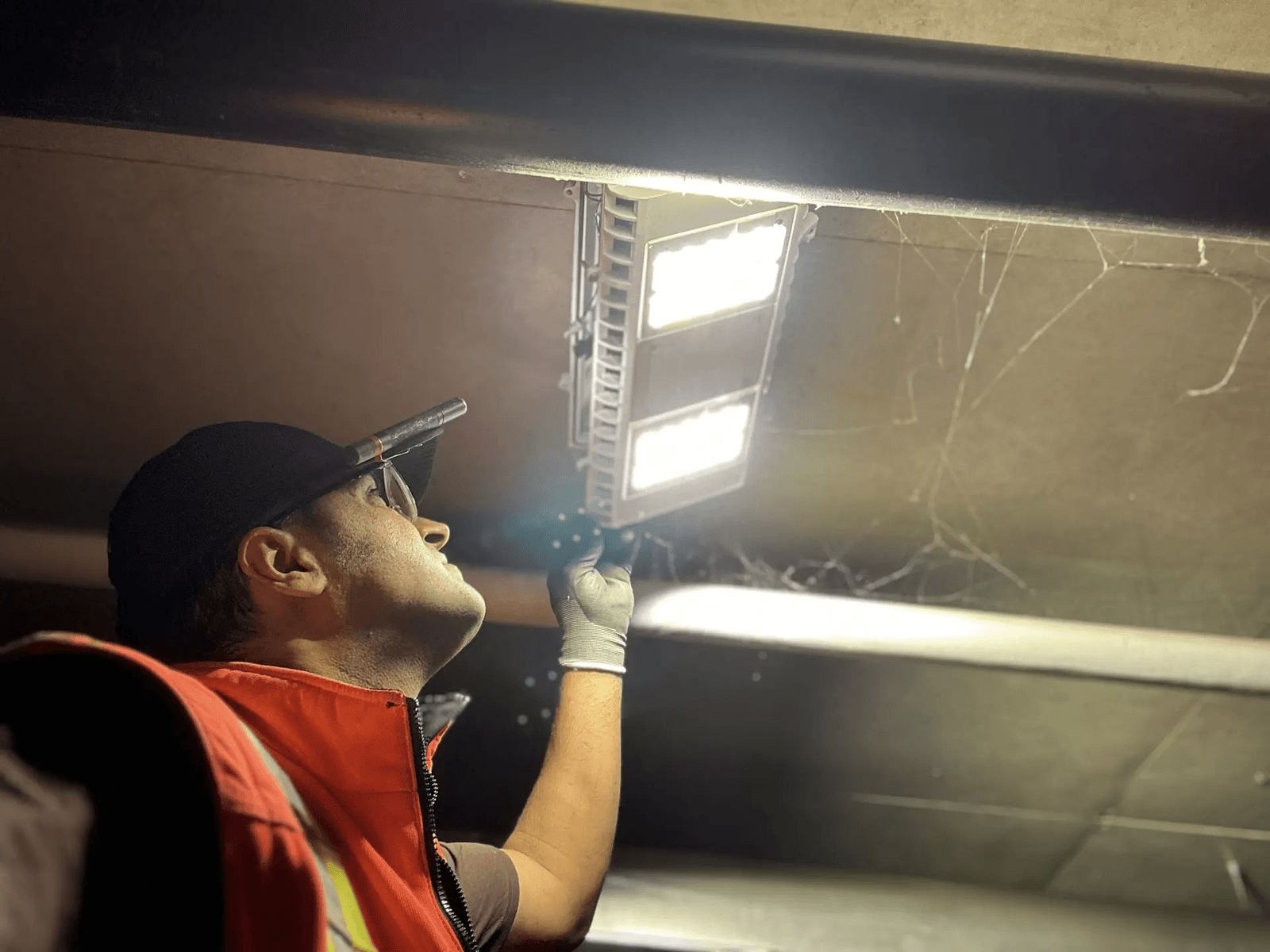 Electrician inspecting or repairing a ceiling LED light fixture in a dark area with headlamp and safety gloves.