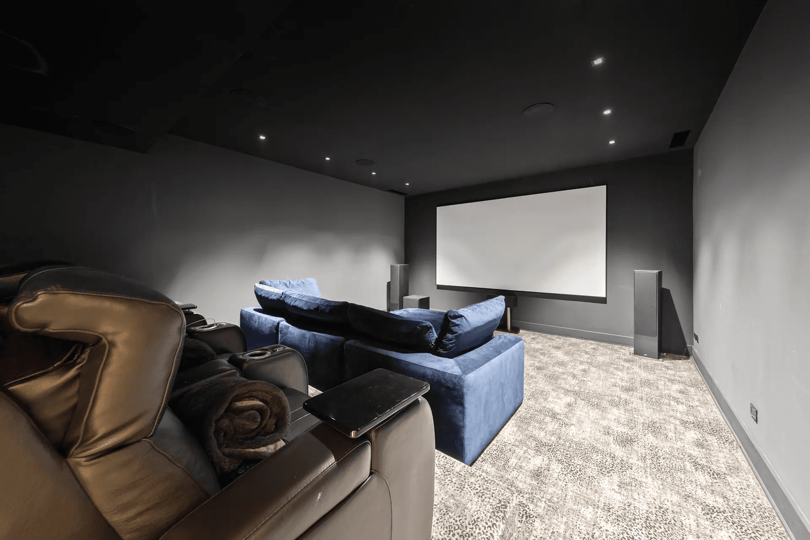 Modern home theatre with large projection screen, surround sound system, blue sofa, leather reclining chairs and recessed lighting