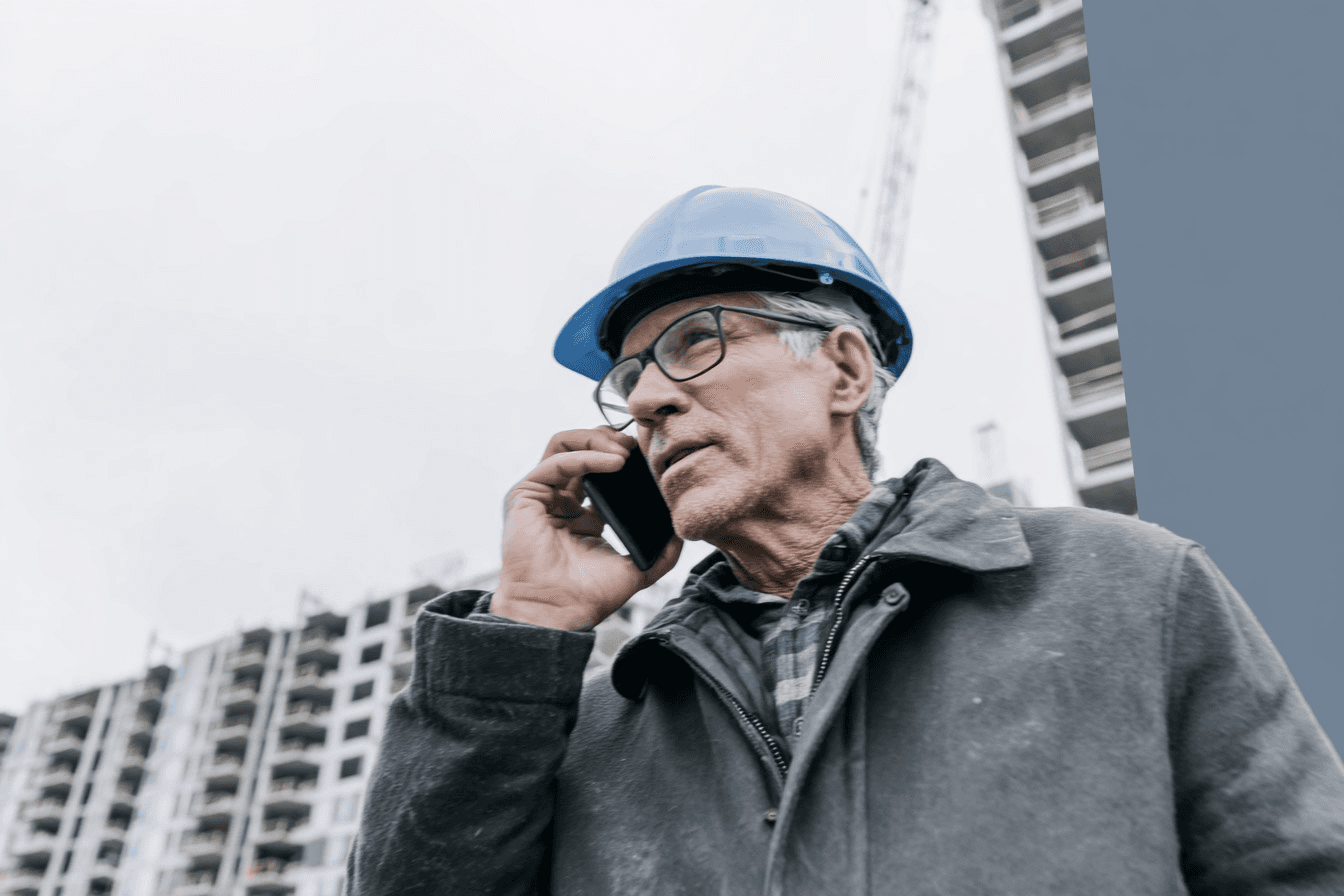 Construction professional wearing a safety helmet and talking on a phone at a building site.