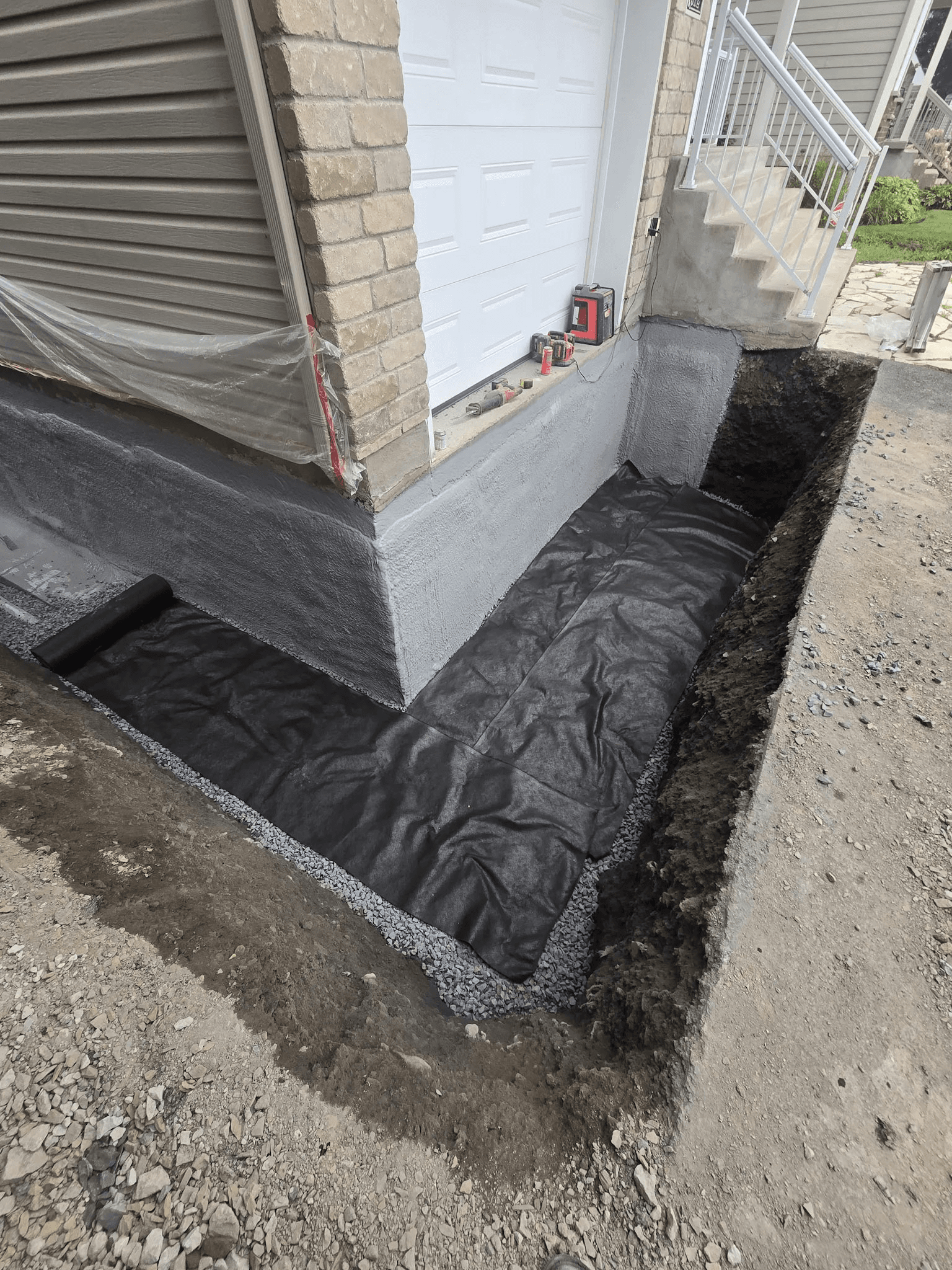 Waterproofing and drainage work around an excavated residential foundation with protective membrane and crushed stone base