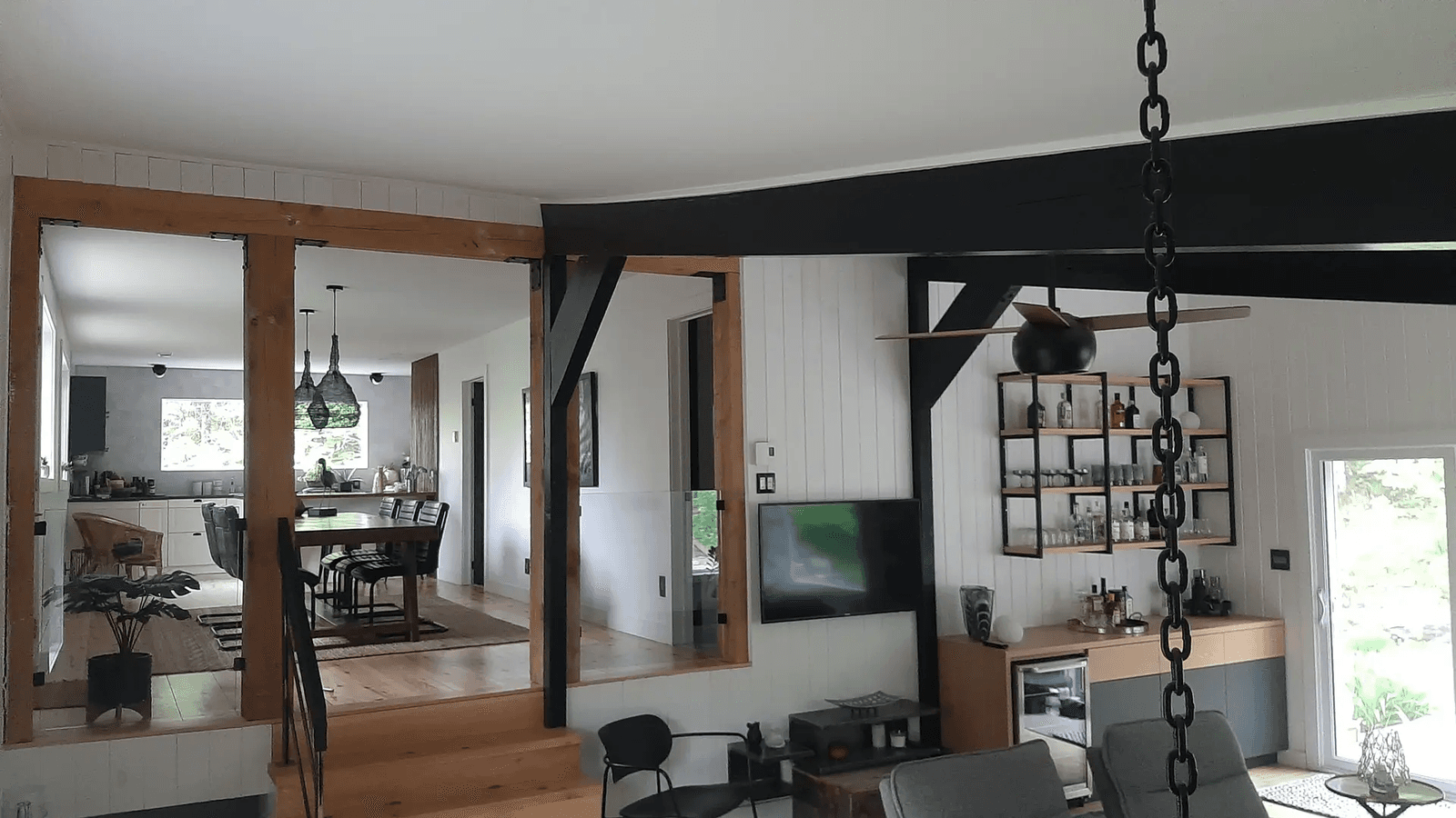 Renovated home interior with exposed wood beams, black structural framing, living room, dining area and modern kitchen in an open-concept space
