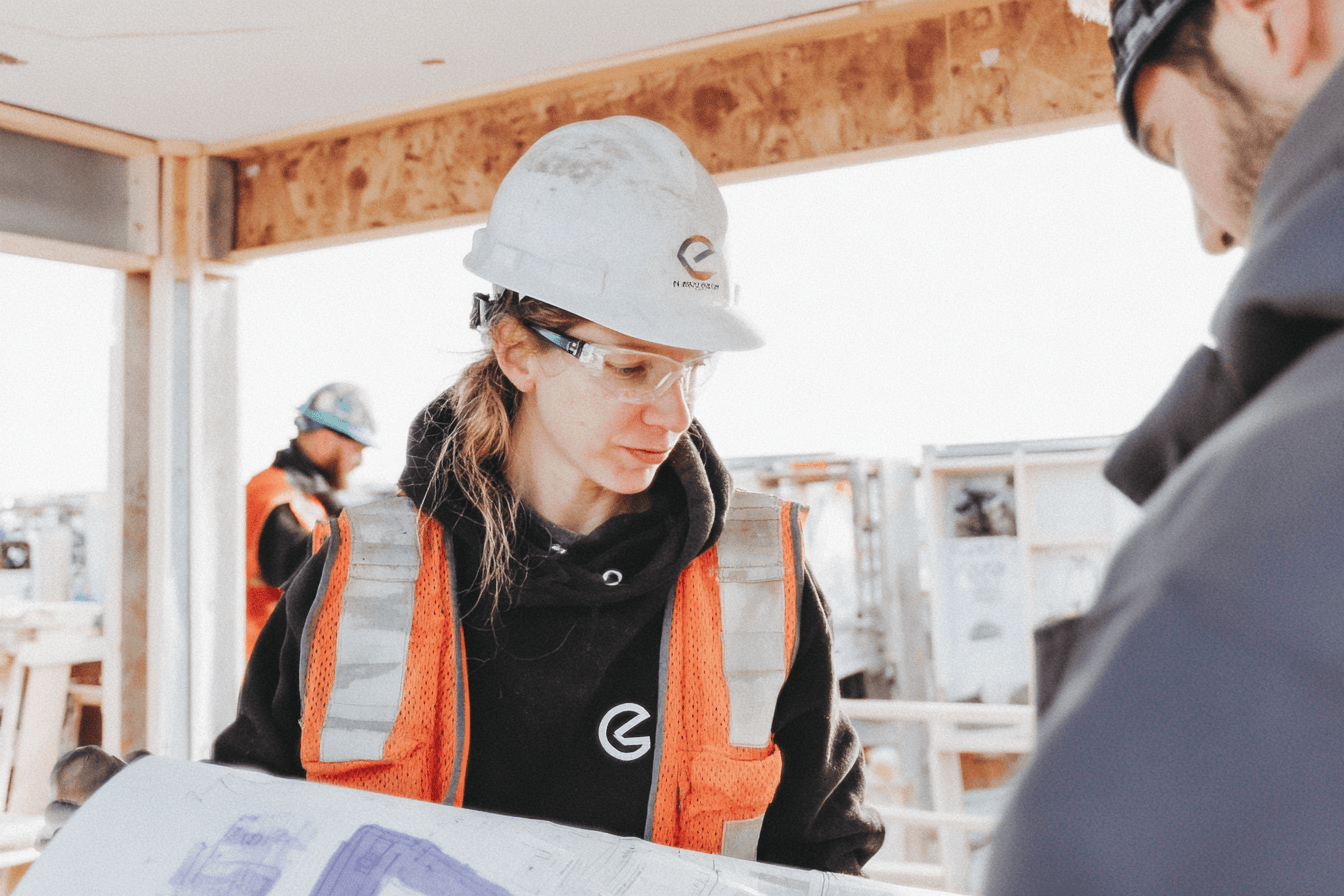 Construction professional wearing a hard hat, safety glasses and a high-visibility vest while reviewing plans on a job site