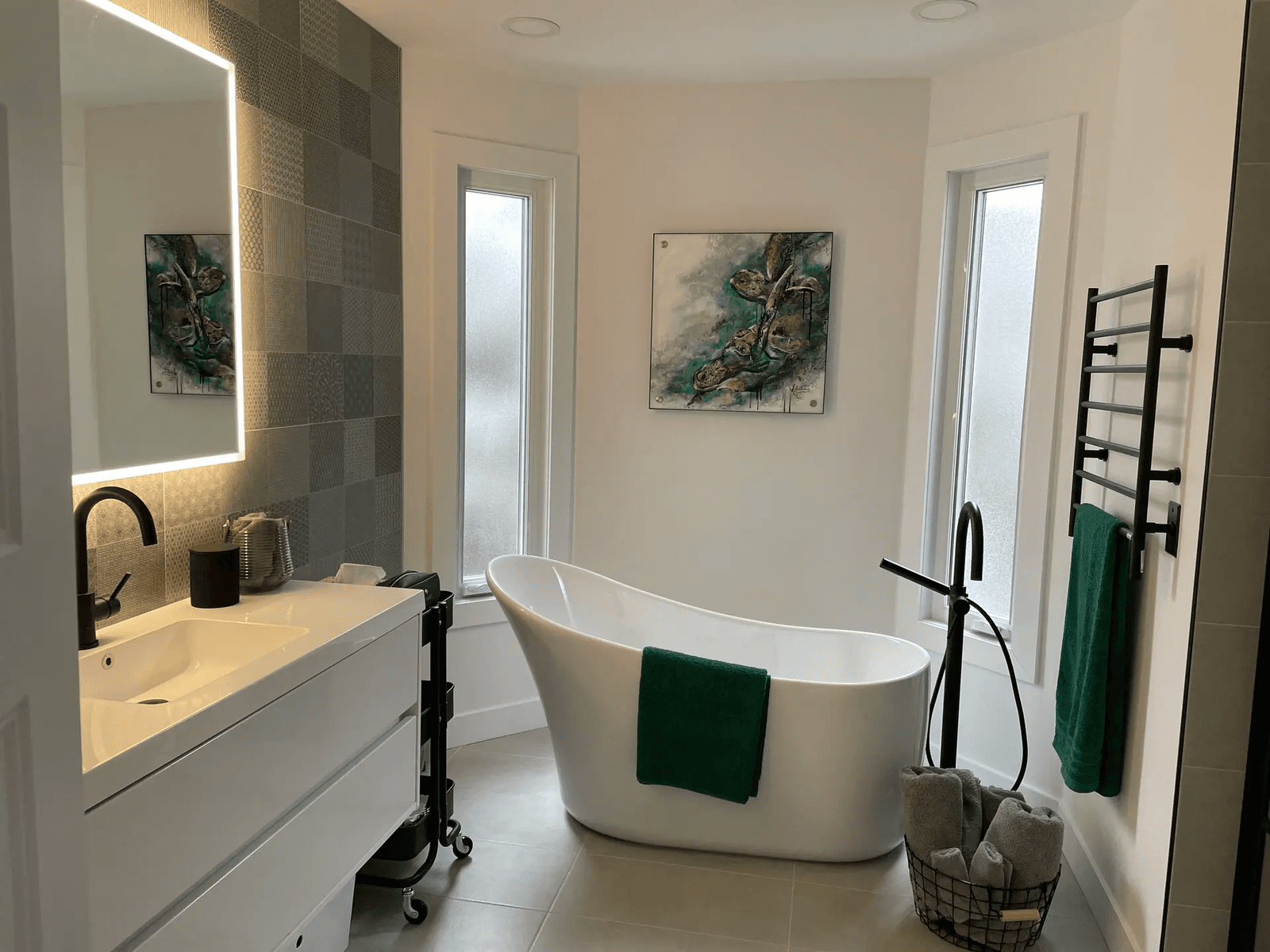 Modern bathroom with white freestanding bathtub, vanity, illuminated mirror, black faucets and tall vertical windows